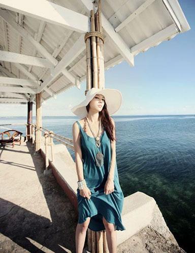 海蓝色的连衣裙，材质飘逸柔软，适合在海边度假时穿着，夸张的饰品带出浓郁的民族风，白色宽檐草帽必不可少。 
